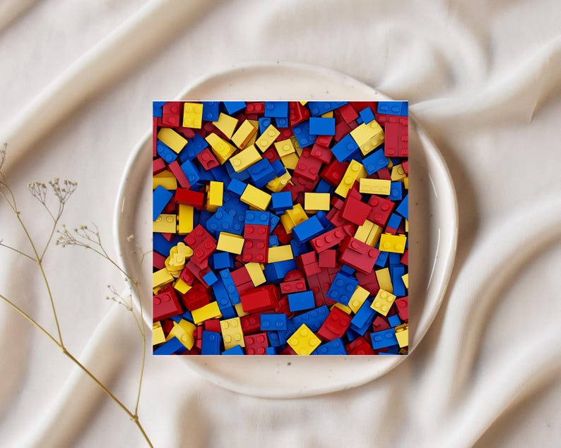 May include: A square image of a white plate filled with a colorful assortment of red, yellow, and blue toy building blocks. The blocks are scattered, creating a vibrant and playful scene. The plate sits on a white, textured surface.