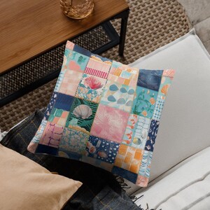 May include: Square decorative pillow with a patchwork design. The pillow features various fabric squares in shades of blue, pink, orange, and white, with seashell and floral patterns. The pillow is placed on a gray and white surface.