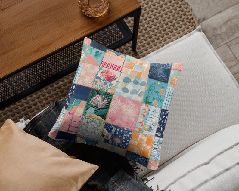 May include: Square decorative pillow with a patchwork design. The pillow features various fabric squares in shades of blue, pink, orange, and white, with seashell and floral patterns. The pillow is placed on a gray and white surface.