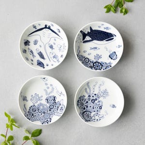 May include: A set of four white ceramic plates featuring intricate dark blue illustrations of marine life, including a manta ray, a whale shark, sea turtles, various fish, and detailed coral reef patterns with circular motifs.