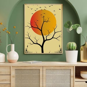 Könnte beinhalten: Ein gerahmter Kunstdruck mit einer schwarzen Baumsilhouette vor einer orange-gelben Sonne und fliegenden Vögeln. Das Kunstwerk wird über einem Holzschrank mit Vasen und einem Kaktus ausgestellt.