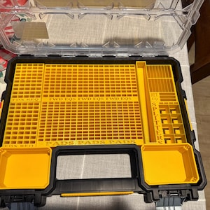 May include: A black and yellow organizer with a clear lid. The interior features a grid-like pattern with labeled compartments for pads and splitters. The handle is black, and the overall design is rectangular.