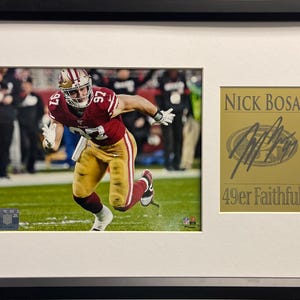 Puede incluir: Una foto enmarcada de un jugador de fútbol americano con un uniforme rojo y dorado corriendo con el balón. La foto está firmada por Nick Bosa con el texto "49er Faithful".