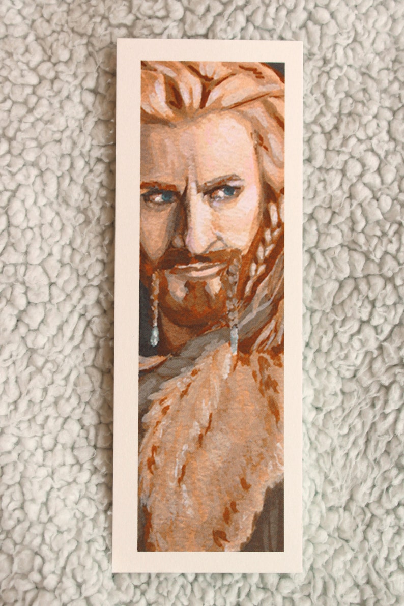 Bookmark print of older dwarf brother painted in gouache. Bookmark is on top of a plain background of a white blanket.