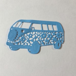 May include: A light blue paper die-cut in the shape of a vintage camper van. The body of the van features an intricate, cut-out leopard print pattern throughout the side panels, with detailed outlines for the wheels, windows, and front headlight.