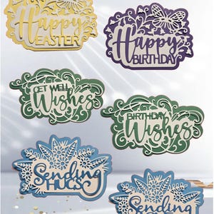 May include: A collection of layered paper cutouts with various greetings. The cutouts include phrases like "Happy Easter," "Happy Birthday," "Get Well Wishes," "Birthday Wishes," "Sending Hugs," and "Sending Love." Each cutout features intricate floral and butterfly designs.