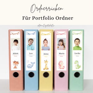 May include: Five colourful portfolio binders with children's photos and names. Each binder has a different colour: peach, light blue, yellow, pink, and green. The text on the binders reads "Ordnerrücken Für Portfolio Ordner" and "Atomic Digital ArtCo."