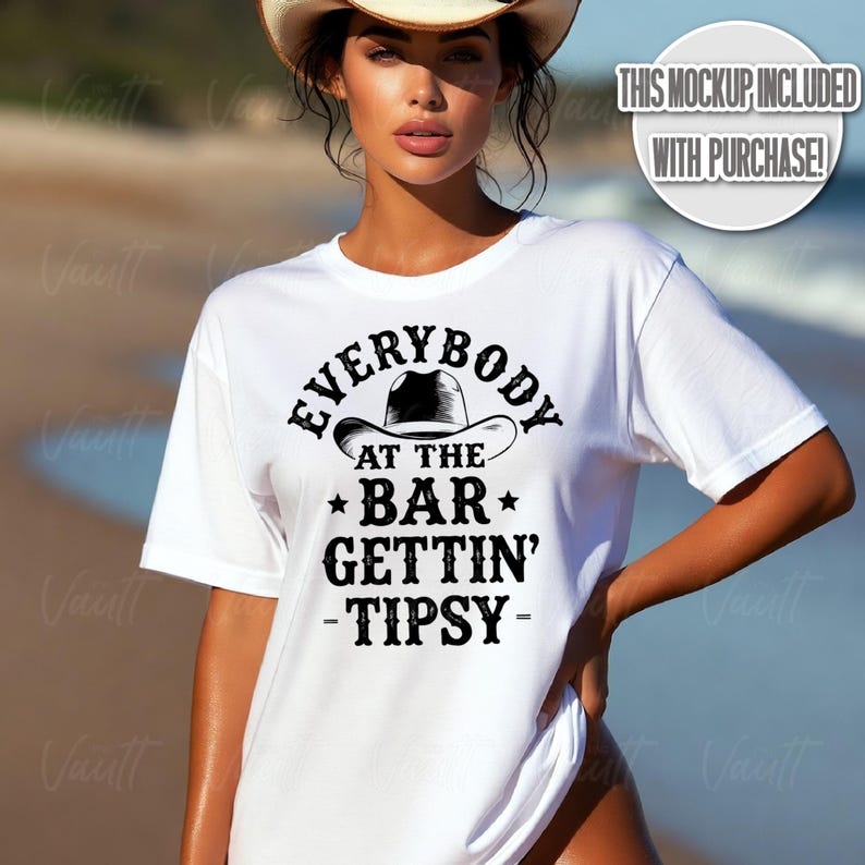 May include: White t-shirt with the text "EVERYBODY AT THE BAR GETTIN' -TIPSY-" in black. The design includes a cowboy hat graphic. The shirt is a short-sleeved crew neck.