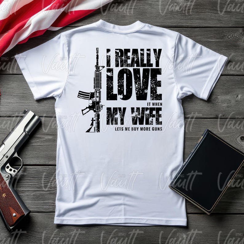 Peut inclure: T-shirt blanc avec un dessin noir d'un fusil et le texte "I REALLY LOVE IT WHEN MY WIFE LETS ME BUY MORE GUNS." Un pistolet et un livre sont &eacute;galement visibles.
