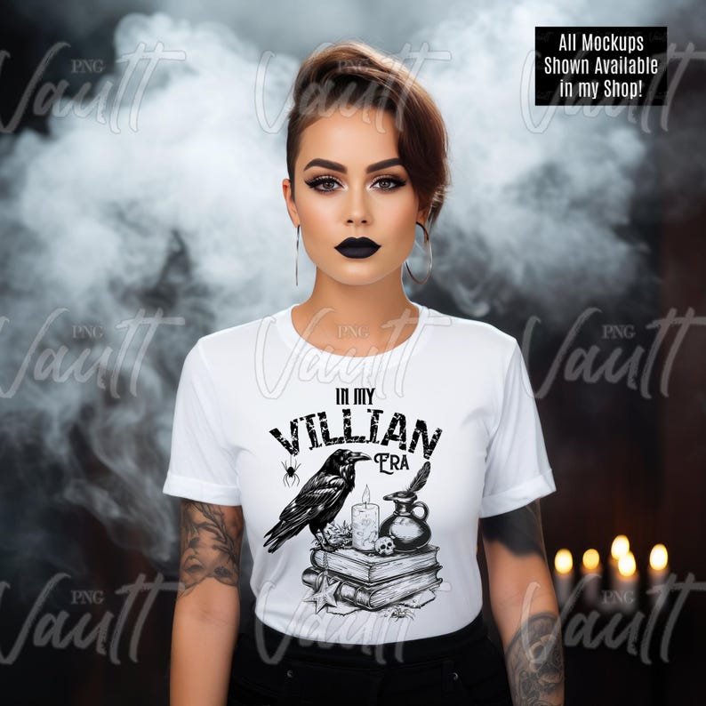 Puede incluir: Una camiseta blanca con un dise&ntilde;o gr&aacute;fico en blanco y negro que presenta un cuervo, una vela, una pluma y una pila de libros. El texto "In My Villian Era" est&aacute; impreso en la camiseta.