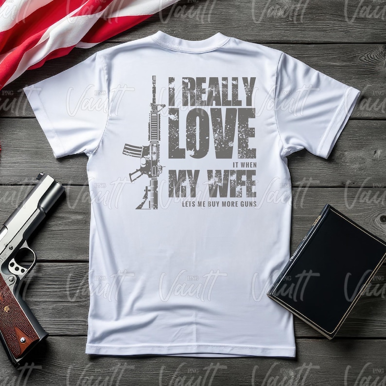 Peut inclure: T-shirt blanc avec un dessin gris d'un fusil et le texte : "I REALLY LOVE IT WHEN MY WIFE LETS ME BUY MORE GUNS." Un pistolet et un livre sont &eacute;galement visibles.