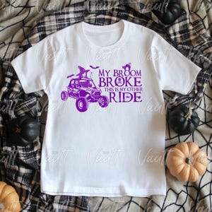 May include: White t-shirt with a purple graphic of a Halloween-themed off-road vehicle with the text "My Broom Broke This Is My Other Ride".