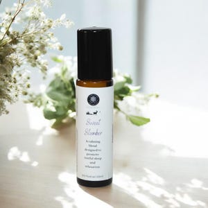 May include: A brown glass roller bottle with a black cap and a white label that reads "Sweet Slumber". The label also includes the text "A calming blend designed to promote restful sleep and relaxation. 1/3 Fluid oz (10ml)"