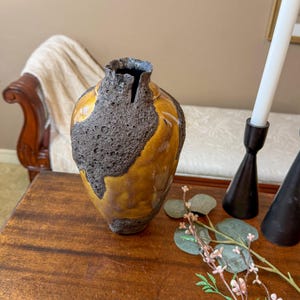 May include: A handcrafted ceramic vase with a unique textured design. The vase features a dark brown, porous exterior contrasted with a glossy, golden-yellow glaze. The opening has a dark blue rim. Decorative home decor.