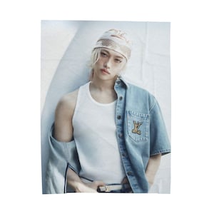 May include: A person wearing a white tank top and a light blue denim shirt with a logo on the pocket. The person is also wearing a patterned headscarf and a belt with a logo.