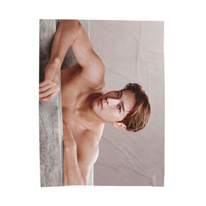 Puede incluir: Retrato de estudio de una persona de piel clara, apoyada contra una pared gris. La persona está sin camisa, con cabello castaño y una expresión concentrada. El fondo es de un color suave y neutro.
