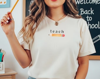 May include: A cream-coloured t-shirt featuring the word "teach" and a pencil illustration. The person is holding a pencil. A chalkboard in the background displays "Welcome Back to School".