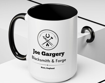 May include: A white ceramic mug with a black interior, handle, and rim. The mug features a circular logo with blacksmith tools and the text "Joe Gargery Blacksmith & Forge, Kent, England."