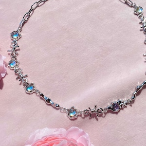May include: A silver necklace with iridescent stones and a delicate chain. The necklace features a unique design with small, intricate details.