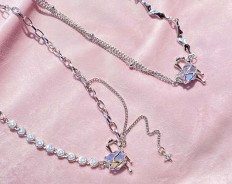 May include: Two silver necklaces with iridescent heart-shaped charms. One necklace has a delicate chain with a star charm and a row of small pearl-like beads. The other necklace has a thicker chain with a more intricate design.