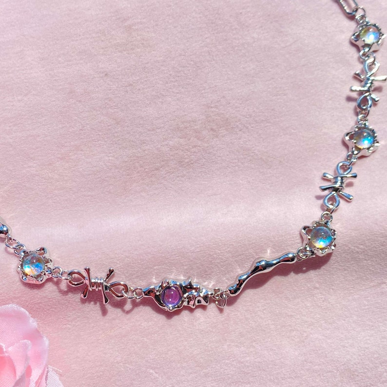 May include: A silver necklace with iridescent and purple gemstones, featuring a barbed wire design.