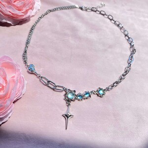Op de afbeelding: Een zilveren ketting met een ster hanger en iriserende blauwe stenen. De ketting heeft een hartvormige sluiting.