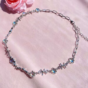 May include: A silver necklace with a delicate chain and iridescent moonstone accents. The necklace features a unique design with small silver knots and a wavy silver bar.
