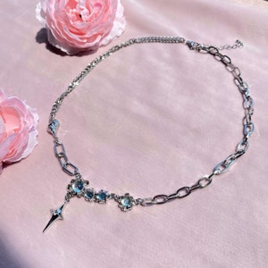 Op de afbeelding: Een zilveren ketting met een zilveren hanger met een stervormig ontwerp en iriserende stenen. De ketting heeft een dik kettinglinkontwerp.