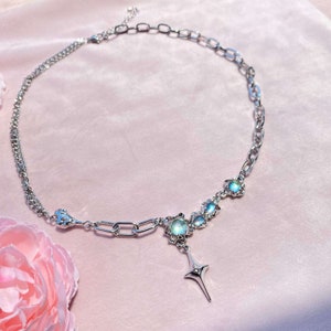 Op de afbeelding: Een zilveren ketting met een ster hanger en iriserende stenen. De ketting heeft een dubbele ketting ontwerp en een karabijn sluiting.