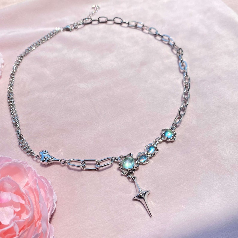 Op de afbeelding: Een zilveren ketting met een ster hanger en iriserende stenen. De ketting heeft een dubbele ketting ontwerp en een karabijn sluiting.
