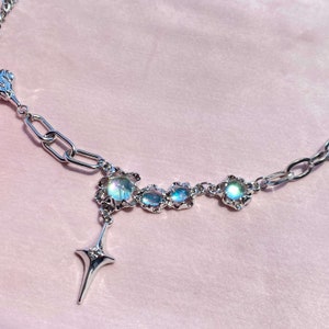 Op de afbeelding: Een zilveren ketting met een ster hanger en iriserende blauwe stenen. De stenen zijn gezet in zilver en hebben een delicaat bloemmotief.