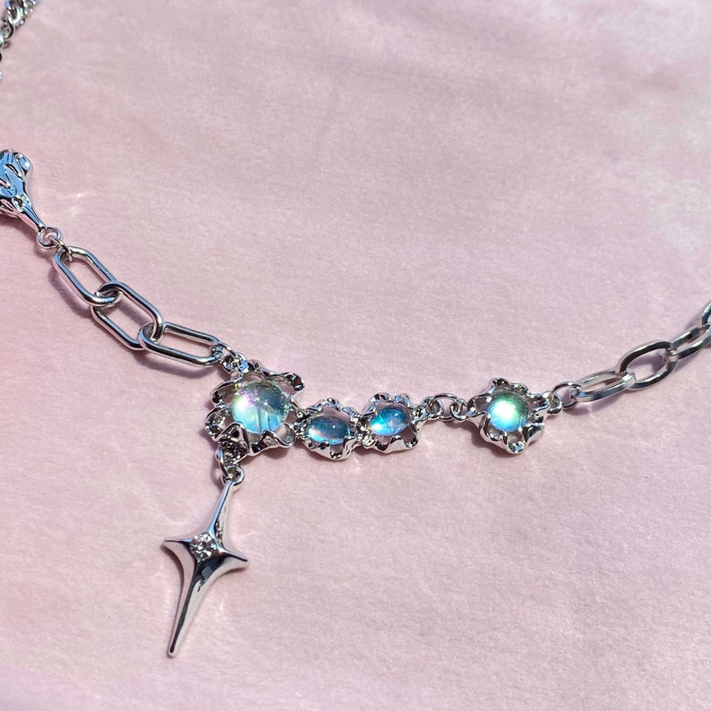 Op de afbeelding: Een zilveren ketting met een ster hanger en iriserende blauwe stenen. De stenen zijn gezet in zilver en hebben een delicaat bloemmotief.