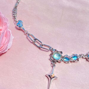 Op de afbeelding: Een zilveren ketting met een ster hanger en iriserende blauwe glazen kralen. De ketting heeft een delicaat ontwerp en is perfect om elke outfit een vleugje glans te geven.
