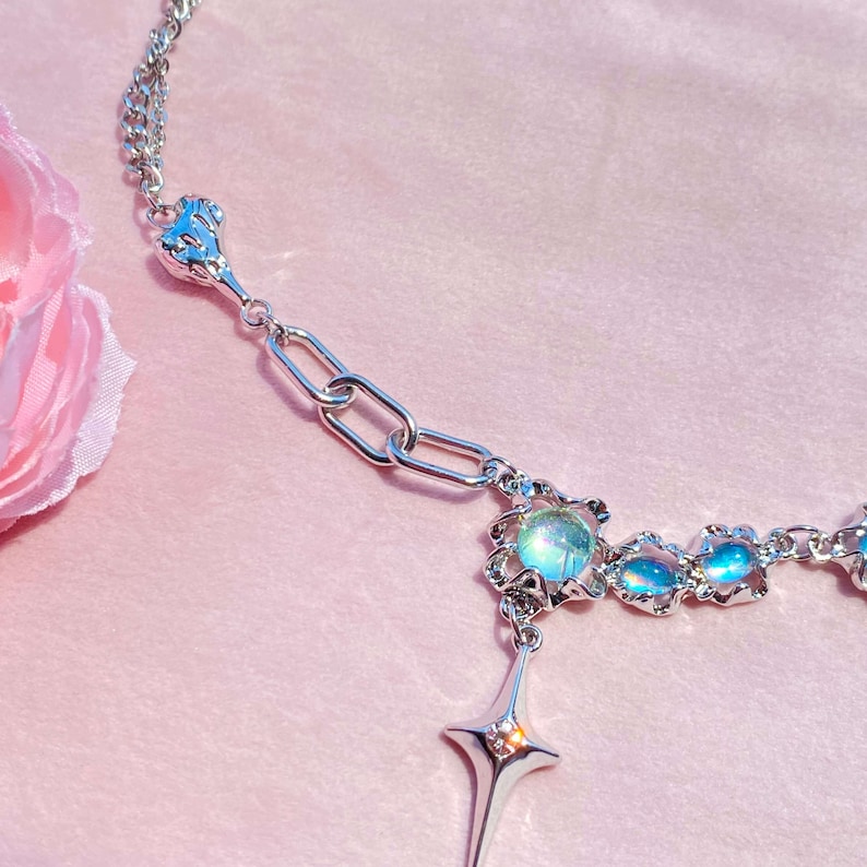 Op de afbeelding: Een zilveren ketting met een ster hanger en iriserende blauwe glazen kralen. De ketting heeft een delicaat ontwerp en is perfect om elke outfit een vleugje glans te geven.