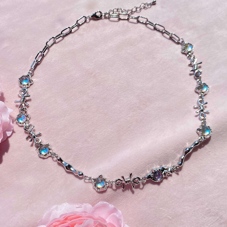 May include: A silver necklace with iridescent stones and a delicate chain. The necklace features a unique design with small, intricate details.