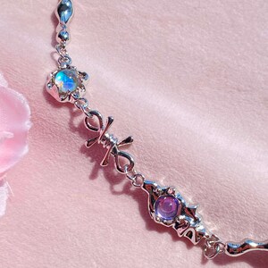 May include: A silver chain necklace with two iridescent gemstones and a barbed wire design. The necklace features a silver chain with a small, iridescent gemstone in a flower-shaped setting, followed by a barbed wire design, and then a larger, iridescent gemstone in a more intricate setting.