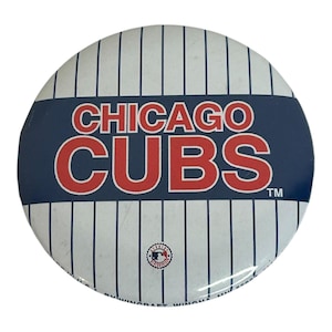 Könnte beinhalten: Runder Chicago Cubs-Button mit weißem Hintergrund und blauen vertikalen Streifen. Die Worte "CHICAGO CUBS" sind in roten Buchstaben auf einem blauen Band. Kleines MLB-Logo unten.