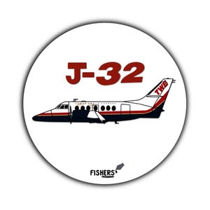 May include: A white circular sticker featuring a stylized illustration of a J-32 airplane with red and black accents. The text "J-32" is in red, and the logo "FISHERS" is at the bottom.
