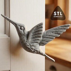 May include: A gray hummingbird sculpture with outstretched wings, mounted on a white surface. The bird's detailed feathers and long beak are visible. The image includes a brown triangle with the text "STL DOWNLOAD".