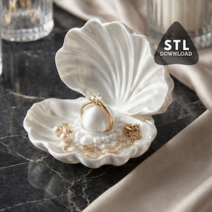 Könnte beinhalten: Eine weiße, muschelförmige Schmuckschale hält einen goldenen Ring mit Diamanten, Perlenohrringe und eine goldene Halskette. Die Schale ist geöffnet und zeigt ein perlenartiges Kissen für den Ring. Der Hintergrund umfasst eine dunkle Marmoroberfläche.