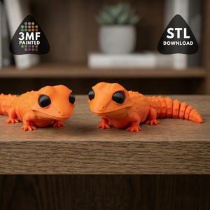 May include: Two orange gecko figurines with black eyes are displayed on a wooden surface. The geckos have detailed scales and articulated tails. The image includes a logo that says "3MF Painted" and "STL Download".