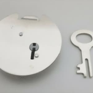 Könnte beinhalten: Ein rundes silberfarbenes Schloss mit einem Schlüsselloch und einem passenden silberfarbenen Schlüssel. Das Schloss hat eine kleine rechteckige Öffnung an der Seite.