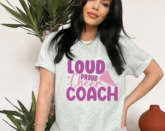 May include: A light grey t-shirt with a purple graphic that says "Loud Proud Cheer Coach" with a pink megaphone graphic.