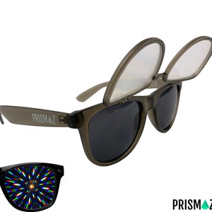Op de afbeelding: Grijze plastic zonnebril met een heldere lens bovenop de donkere lens. De zonnebril heeft het woord "PRISMAZ" aan de zijkant.