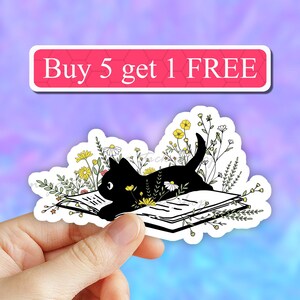 May include: Black cat reading a book surrounded by flowers. The book is open and the cat is laying on top of it. The text "Buy 5 get 1 FREE" is at the top of the image.