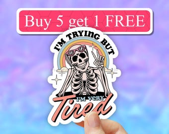 May include: A sticker with a skeleton wearing sunglasses and making a peace sign. The sticker says "I'm trying but I'm very tired" with a rainbow behind the skeleton. The sticker also has a pink banner at the top that says "Buy 5 get 1 FREE".