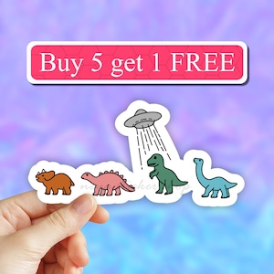 May include: A set of four dinosaur stickers with a UFO showering them. The dinosaurs are a brown triceratops, a pink stegosaurus, a green T-Rex, and a blue brachiosaurus. The text "Buy 5 get 1 FREE" is at the top of the image.