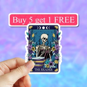 May include: A sticker featuring a tarot card illustration of a skeleton reading a book. The card is blue with purple and yellow flowers and the text "THE READER" at the bottom. The card has three moons in the top left corner.