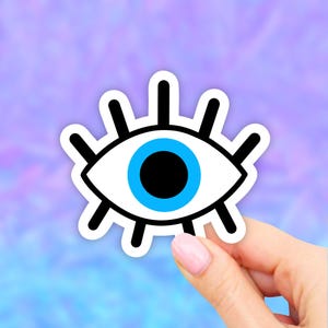 May include: A white sticker with a black outline of an eye with a blue iris and black pupil. The eye has eyelashes.