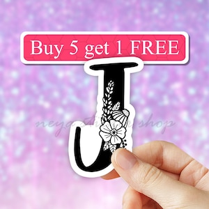 May include: Black and white floral letter J sticker. The sticker has a white floral design on a black letter J. The sticker is on a pink background. The text "Buy 5 get 1 FREE" is on a pink banner above the sticker.